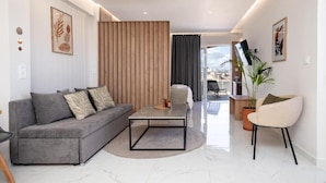 A modern living room with a grey sofa, a coffee table, a chair, and a potted plant. - Anele Luxury Suites (Chania)