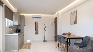 A modern kitchen with a built-in oven, a dining area with a table and chairs, and a coat rack. - Anele Luxury Suites (Chania)