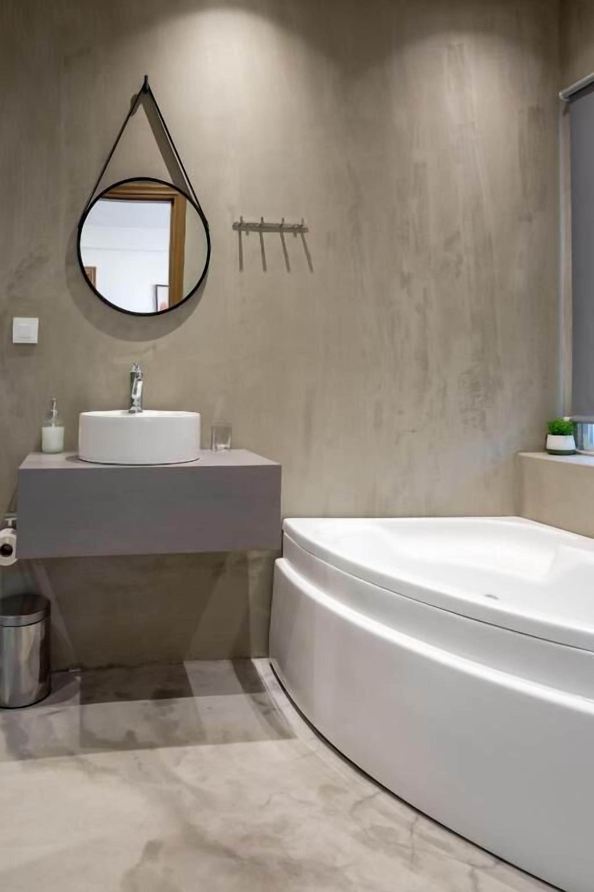 A modern bathroom with a round mirror, a sink, a toilet, and a bathtub.