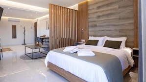 A modern hotel room with a large bed, a wooden headboard, a desk, and a seating area. - Anele Luxury Suites (Chania)