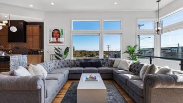 A modern living room with a grey sectional sofa, a coffee table, and large windows offering a view of the outdoors.