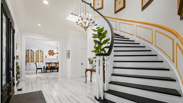 A modern interior with a curved staircase, a chandelier, and a dining area with a white table and chairs. - AL Oasis | Sleeps 12 | Hot Tub | Sauna | Pool Table (Mobile)