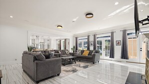 A spacious living room with a grey sectional sofa, a coffee table, and a large window with curtains. - AL Oasis | Sleeps 12 | Hot Tub | Sauna | Pool Table (Mobile)