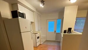 A compact kitchen with white appliances, a wooden floor, and a view through a door.