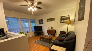 A living room with a sofa, coffee table, and TV, wooden flooring, and a ceiling fan.
