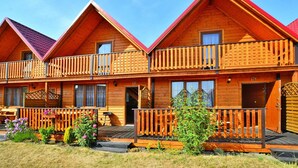 Een rij houten vakantiehuisjes met rode daken, elk met een balkon en een deur met een nummer.