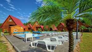 Een resort met houten hutten, een zwembad en ligbedden.