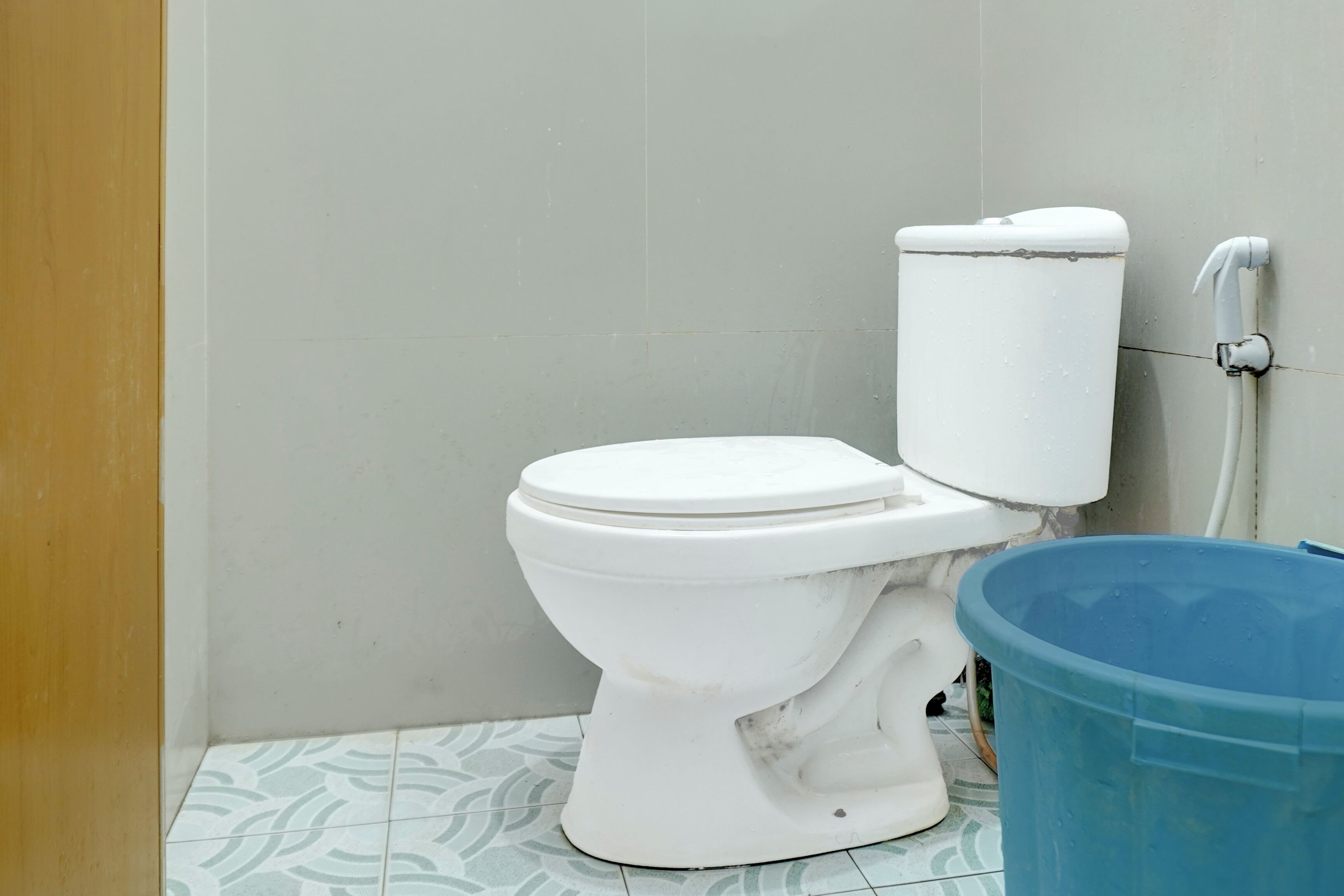 A white toilet with a closed lid in a bathroom with patterned floor tiles.