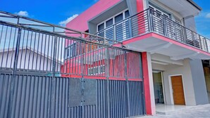 Un edificio moderno de dos pisos, con fachada roja y blanca, un portón de metal y un balcón.