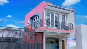 Un edificio de dos pisos con balcón, entrada protegida por un portón y un cartel.