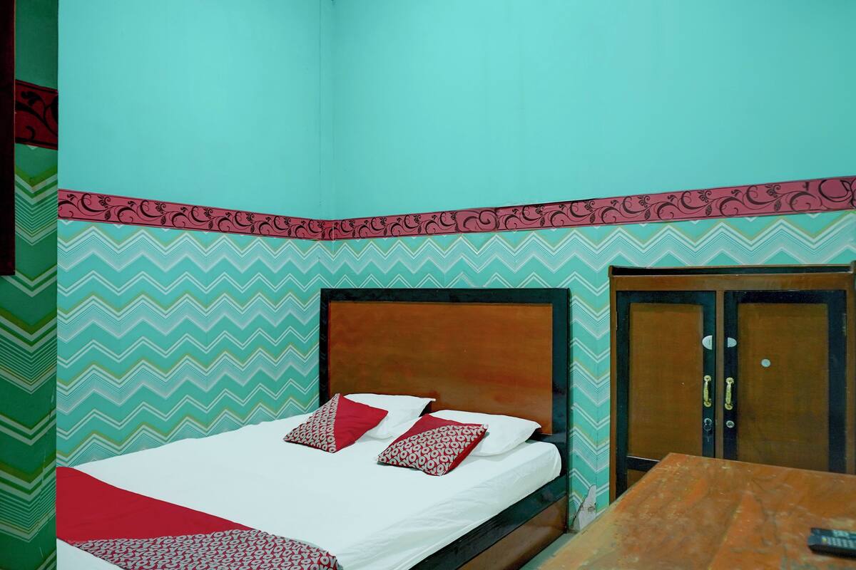 A bed with white bedding and red and white patterned pillows, a wooden headboard, and a wooden wardrobe with a door.