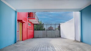 Un patio con piso de baldosas, un edificio rojo con balcón y una pared blanca.