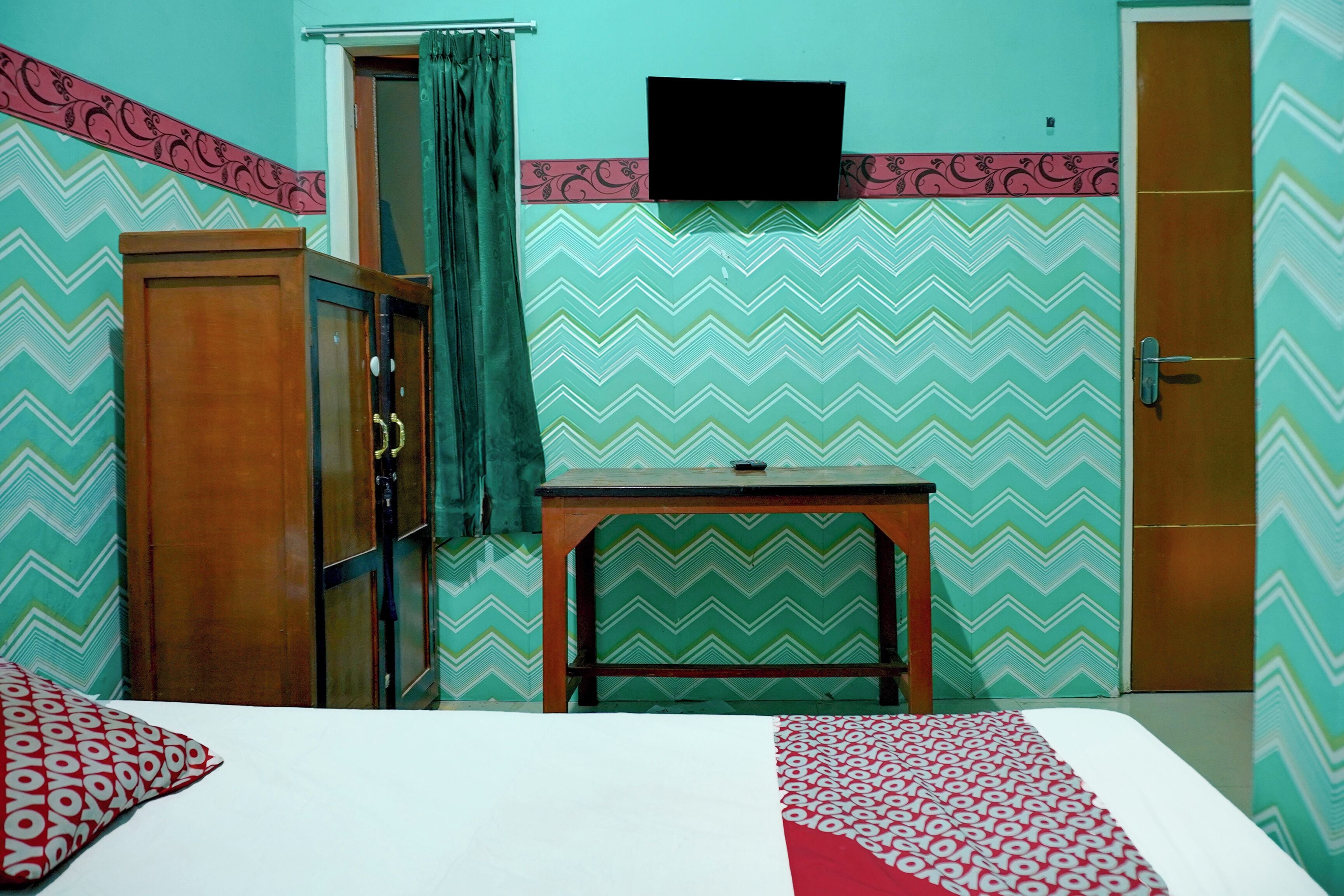 A room with a bed, a wooden wardrobe, a small table, and a door.