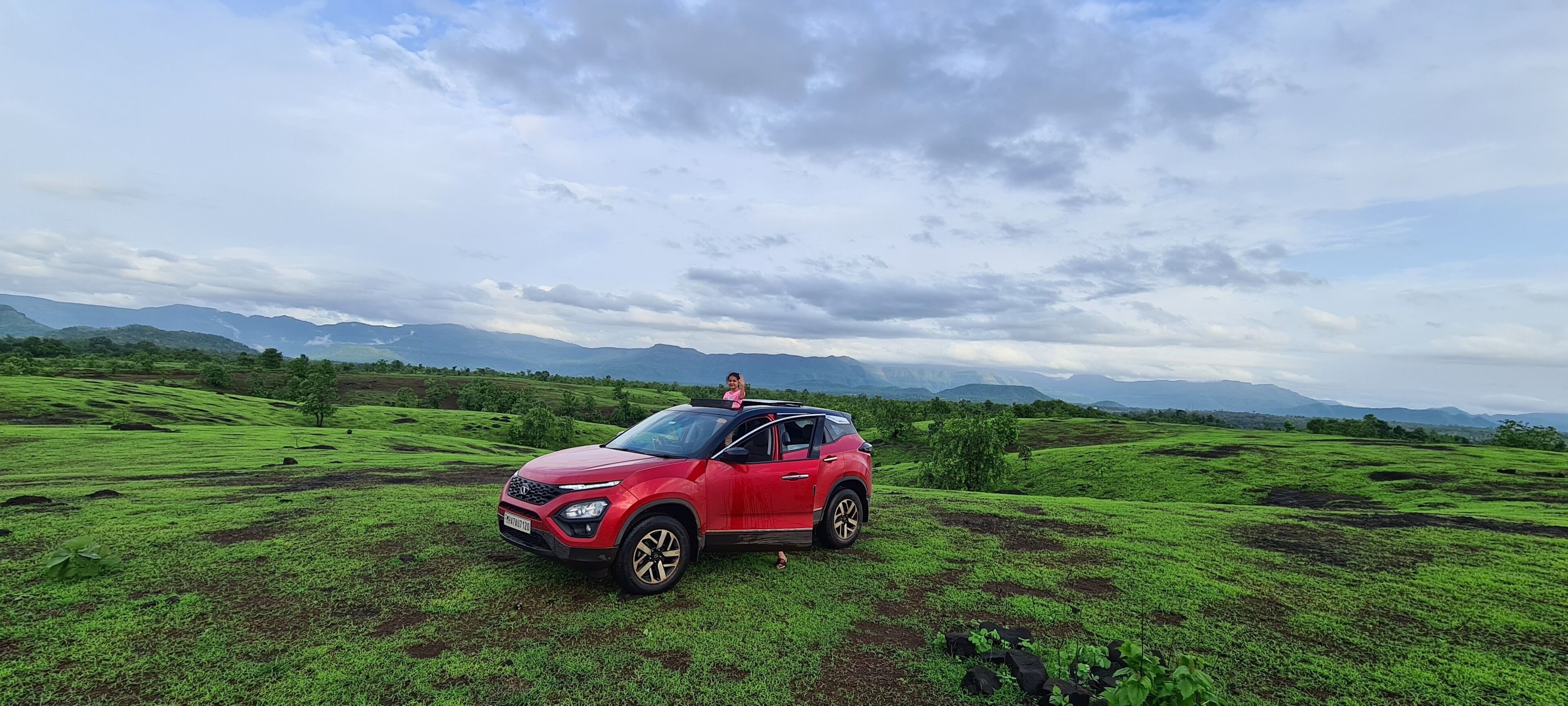 Un SUV rojo estacionado en un campo verde con montañas al fondo.