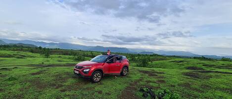 Un SUV rojo estacionado en un campo verde con montañas al fondo.