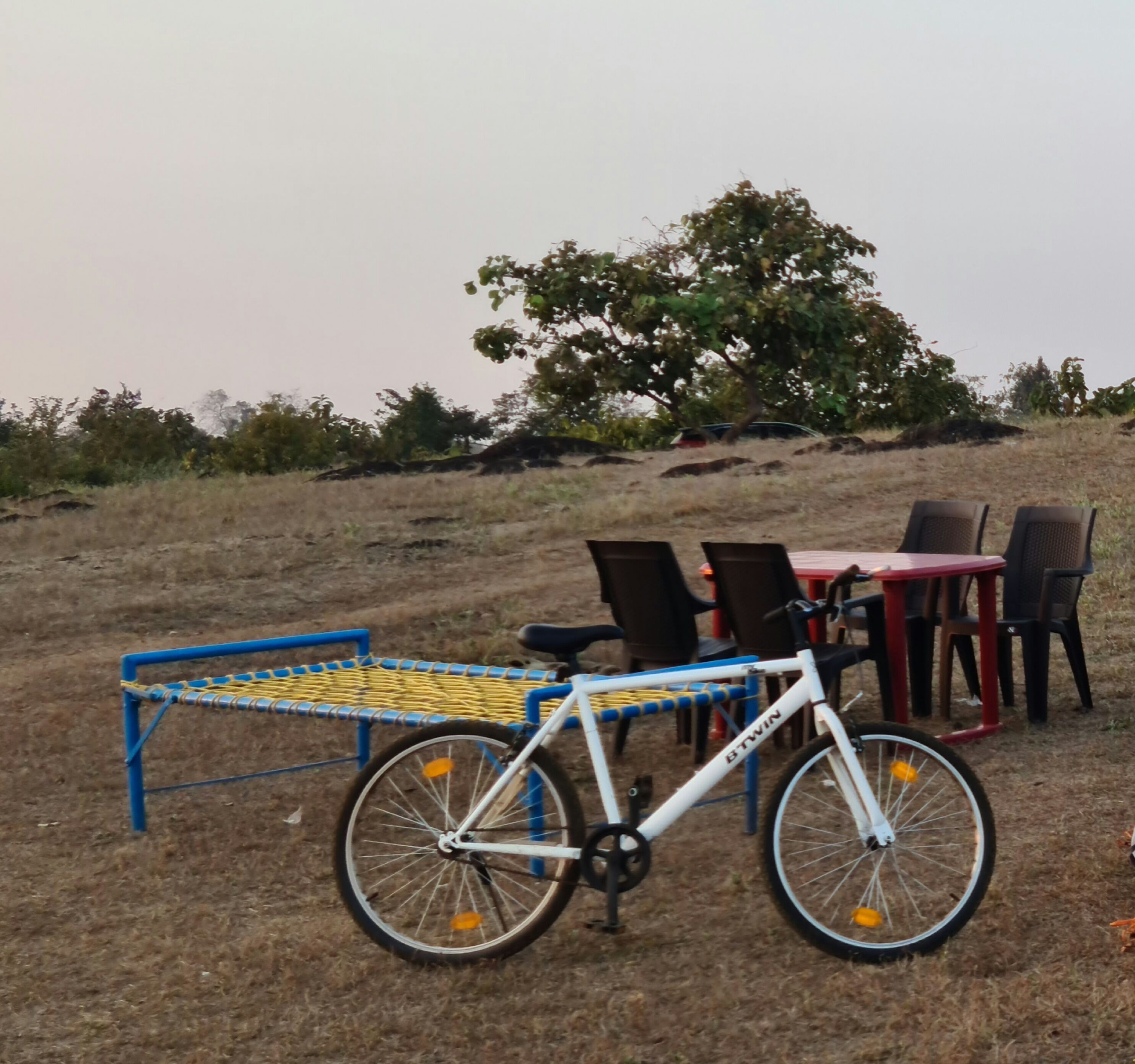 Ein Fahrrad, das neben einer blau-gelben Sitzbank steht, mit Tisch und Stühlen im Hintergrund.