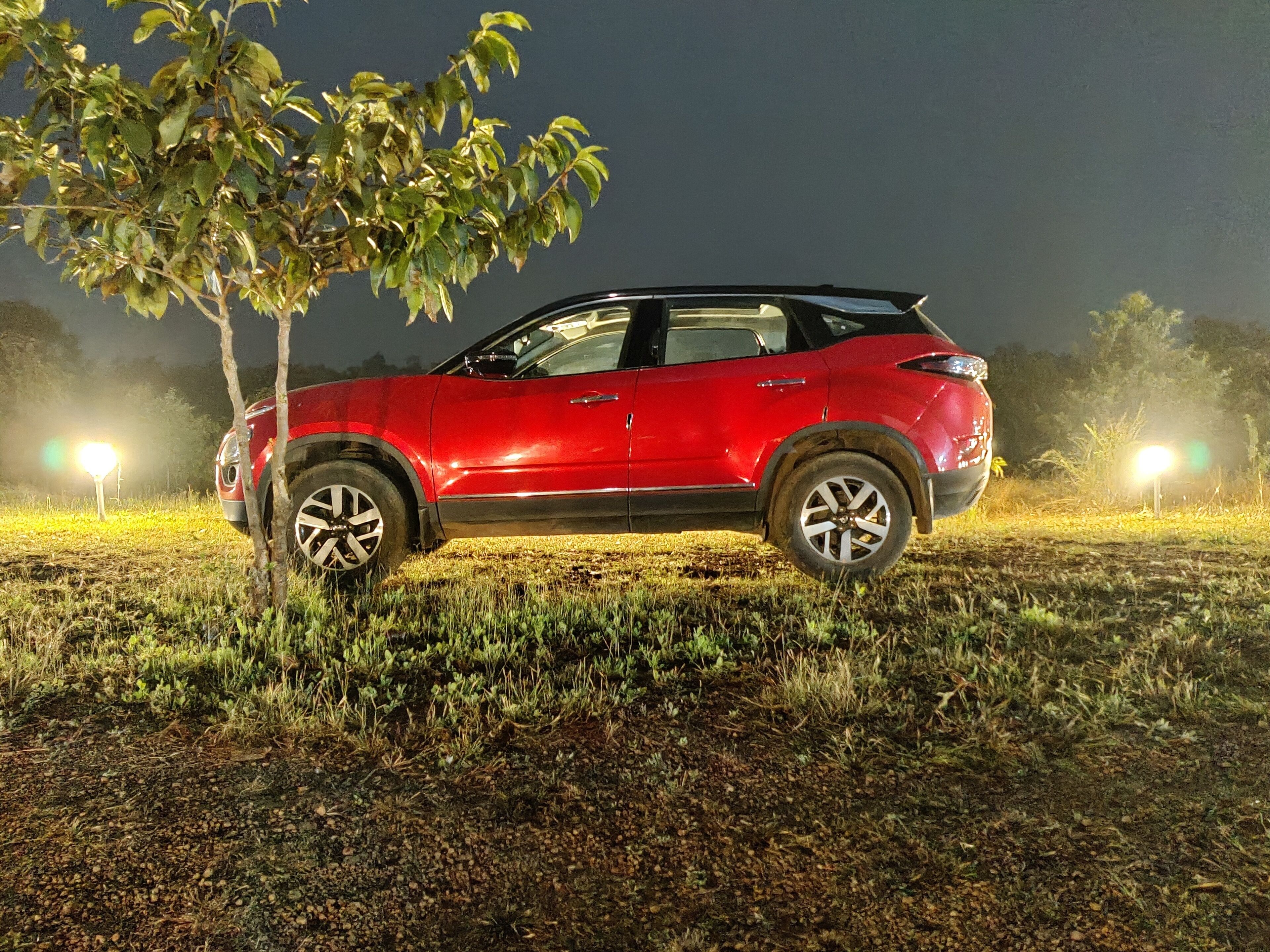 A red SUV parked on a grassy field at night with streetlights in the background.