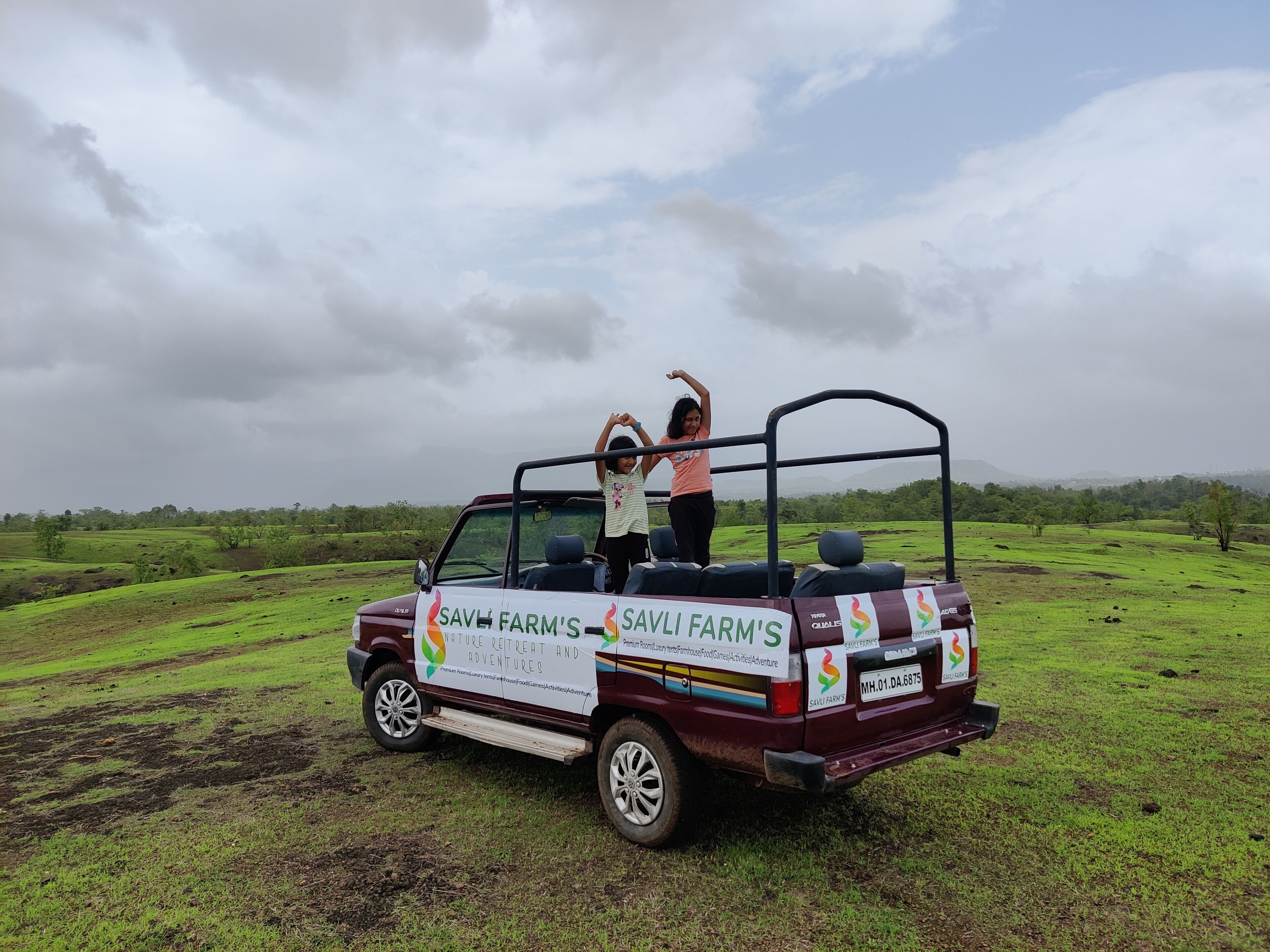 A safari vehicle with "SAVLI FARM'S" branding parked on a grassy field.