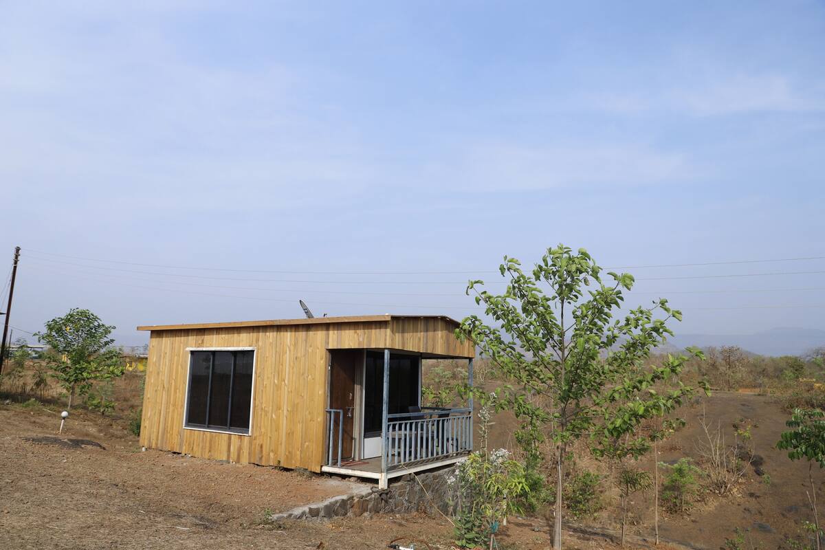 Een klein houten huisje met een balkon, omringd door droge begroeiing en een heldere lucht.