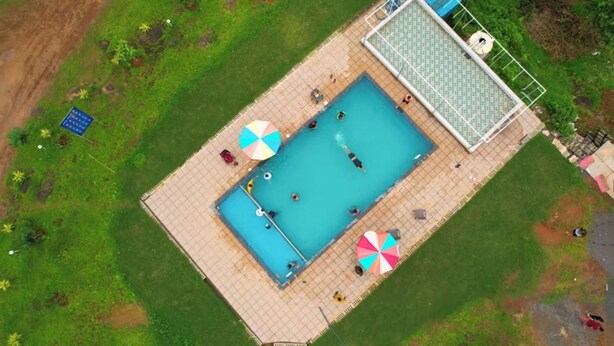 Une vue aérienne d’une piscine rectangulaire, dont le bord est revêtu de carreaux, entourée de pelouse et de quelques arbres.