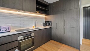 Een moderne keuken met donkere houten kastjes, een witte betegelde spatwand, een roestvrijstalen spoelbak, een magnetron en een inbouwoven.