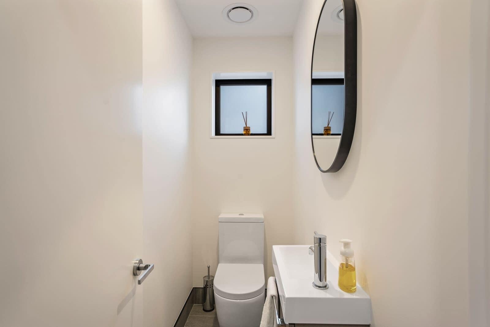 A modern bathroom with a toilet, a sink, a mirror, and a small window.
