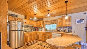 A kitchen with wooden cabinets, a stainless steel refrigerator, a wooden island with stools, and pendant lighting.