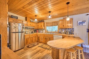 A kitchen with wooden cabinets, a stainless steel refrigerator, a wooden island with stools, and pendant lighting.