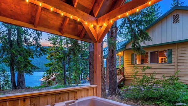 A wooden deck with a hot tub, overlooking a lake and forested area.