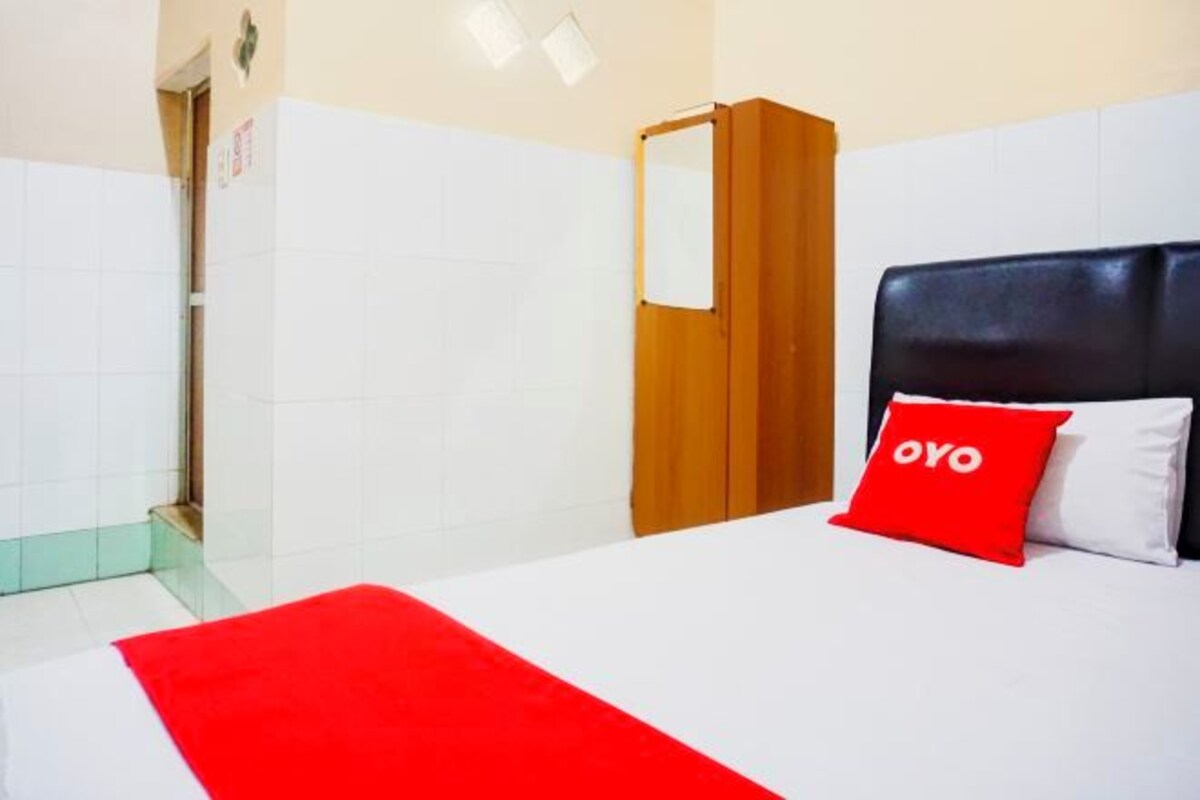 Una habitación de hotel con una cama, una almohada roja, un armario de madera y un espejo.