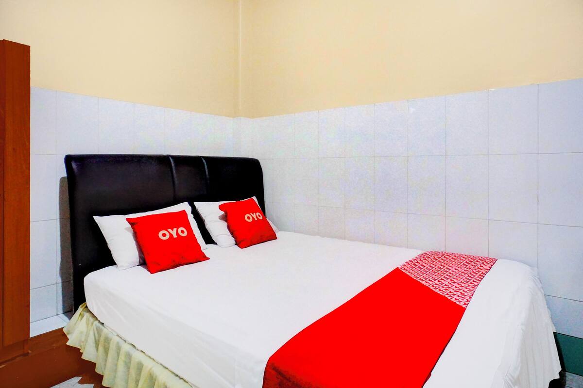 Habitació d'hotel amb un llit, parets blanques i un llençol de llit vermell i blanc.