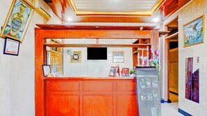 Zona de recepción con mostrador de madera, certificados enmarcados, pantalla digital y vitrina de vidrio.