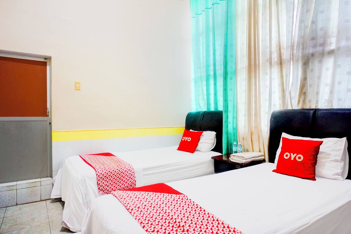 Una habitació d'hotel amb dos llits, cadascun amb un llençol i coixins estampats vermells i blancs amb l'etiqueta “OYO”.