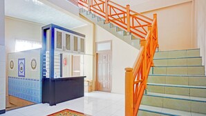 Un vestíbulo de hotel con una recepción, una escalera con barandillas anaranjadas y una alfombra estampada en el suelo.
