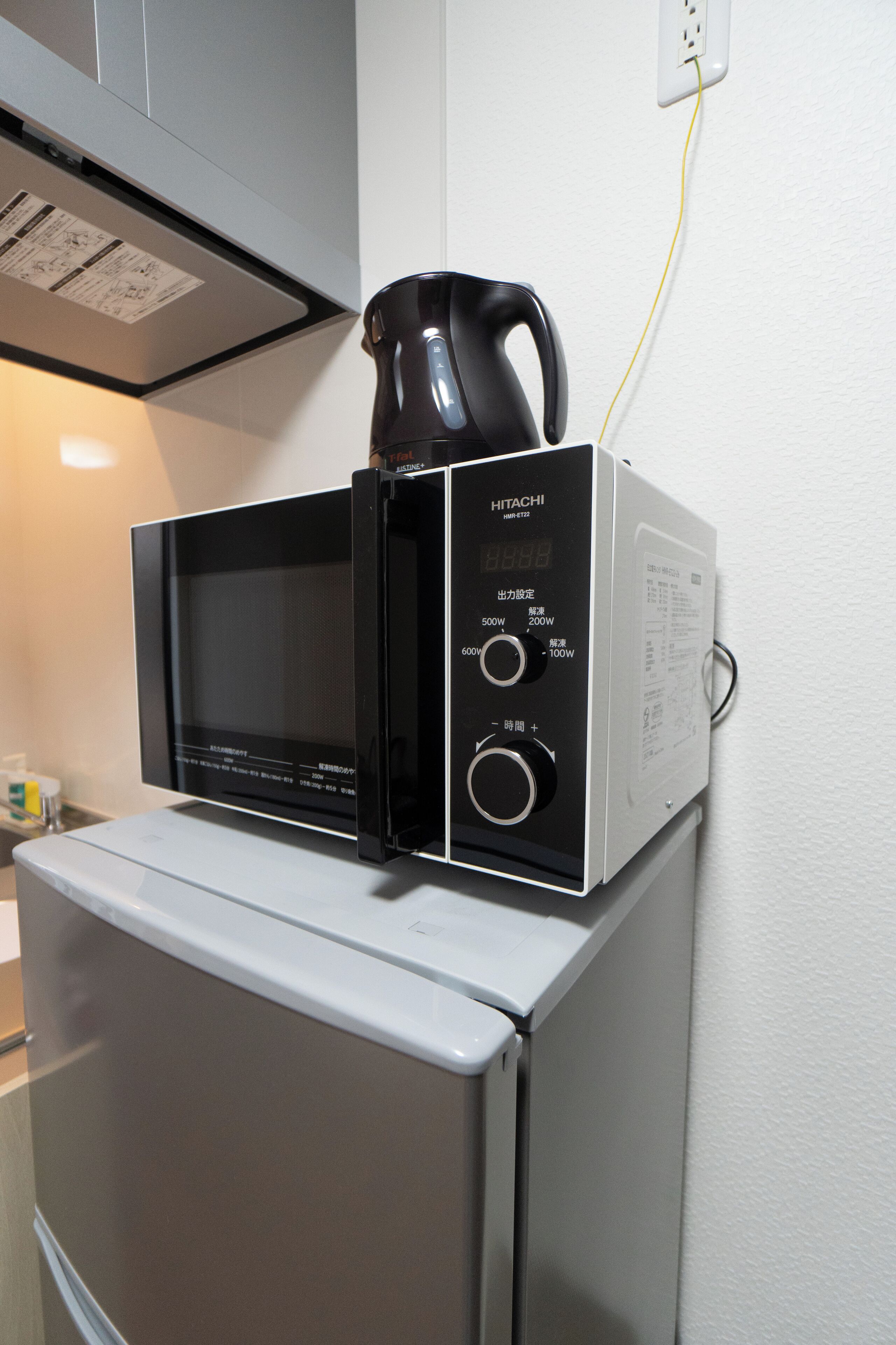 A compact kitchen with a microwave and a kettle on top of a refrigerator.