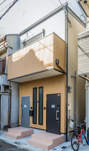 A two-story building with a wooden facade, two doors, and a bicycle parked outside. - HANASTAY SONO (Osaka)