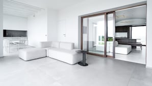 A modern living room with a sectional sofa, a small round table, and a glass door leading to another room. - Villa 'Domo La Vela' with Sea View, Wi-Fi and Air Conditioning (Orosei)