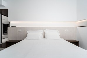 Una habitación de hotel moderna con una cama grande, dos mesitas de noche y un estante empotrado sobre la cama.