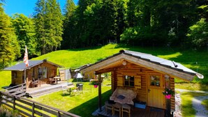 Eine Holzhütte mit einer Terrasse, einer kleinen Veranda und einem Grillbereich.