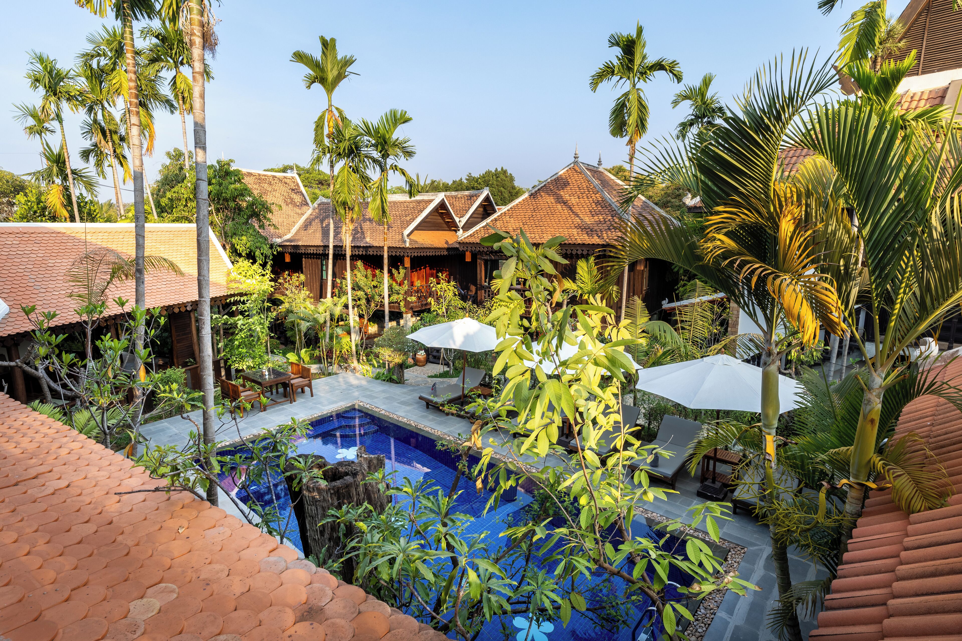 A pool area with a tiled roof, surrounded by palm trees and a building with a tiled roof.
