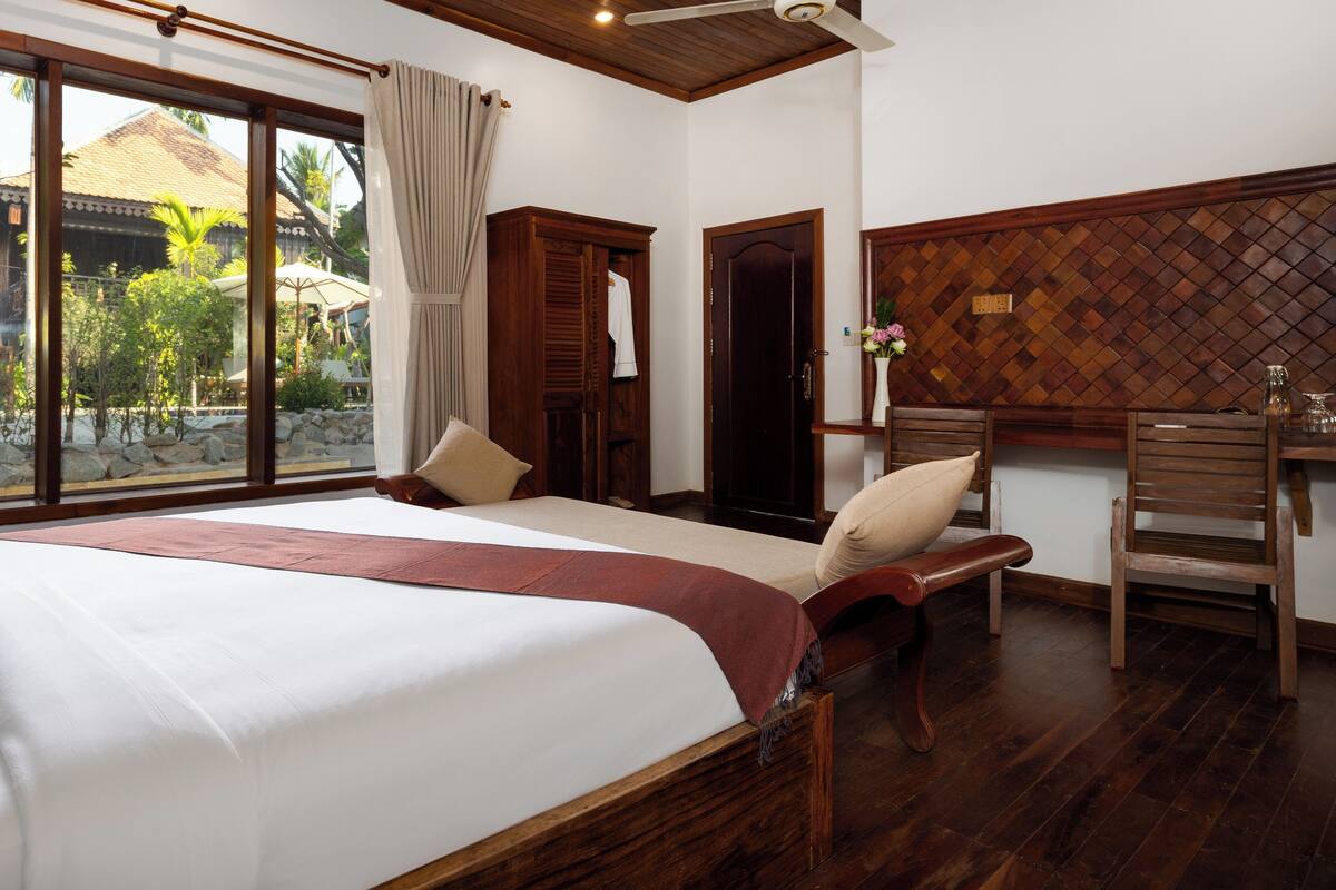 A hotel room with a large bed, wooden furniture, and a view of a traditional building outside.