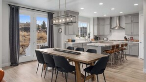 Een moderne keuken met een groot eiland, grijze kastjes, en een eethoek met een houten tafel en stoelen.
