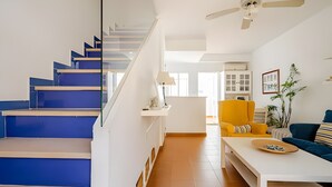 Eine Treppe mit blauen Stufen, eine weiße Wand, ein gelber Sessel, ein blaues Sofa und ein Deckenventilator.