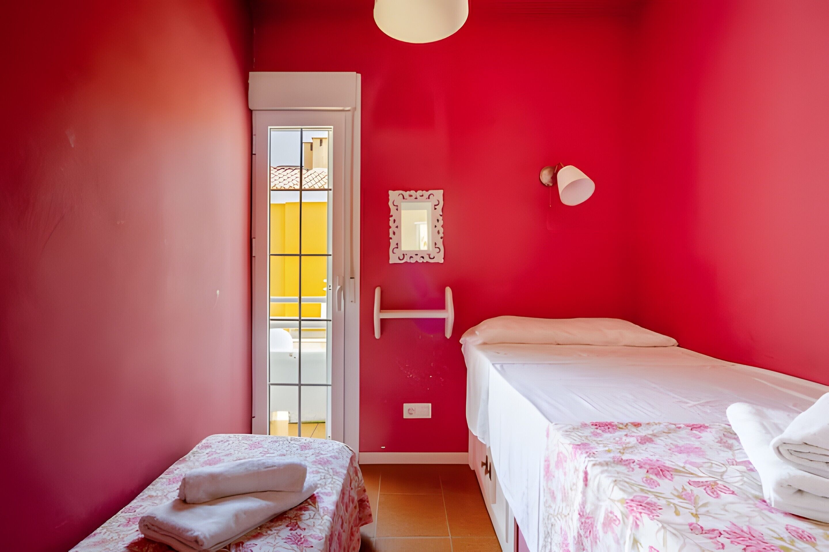 A room with two beds, a door leading outside, and a wall-mounted light fixture.