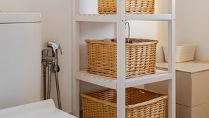 Ein weißes Metallregal mit Korbwannen an einer weißen Wand, neben einer weißen Toilette und einem weißen Schrank.