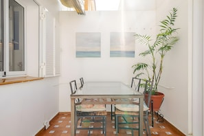 A dining area with a glass table, chairs, a potted plant, and two paintings on the wall.