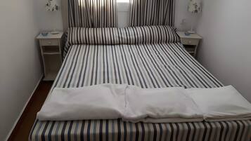 Una cama con ropa de cama a rayas, dos mesitas de noche con lámparas y una ventana con cortinas.