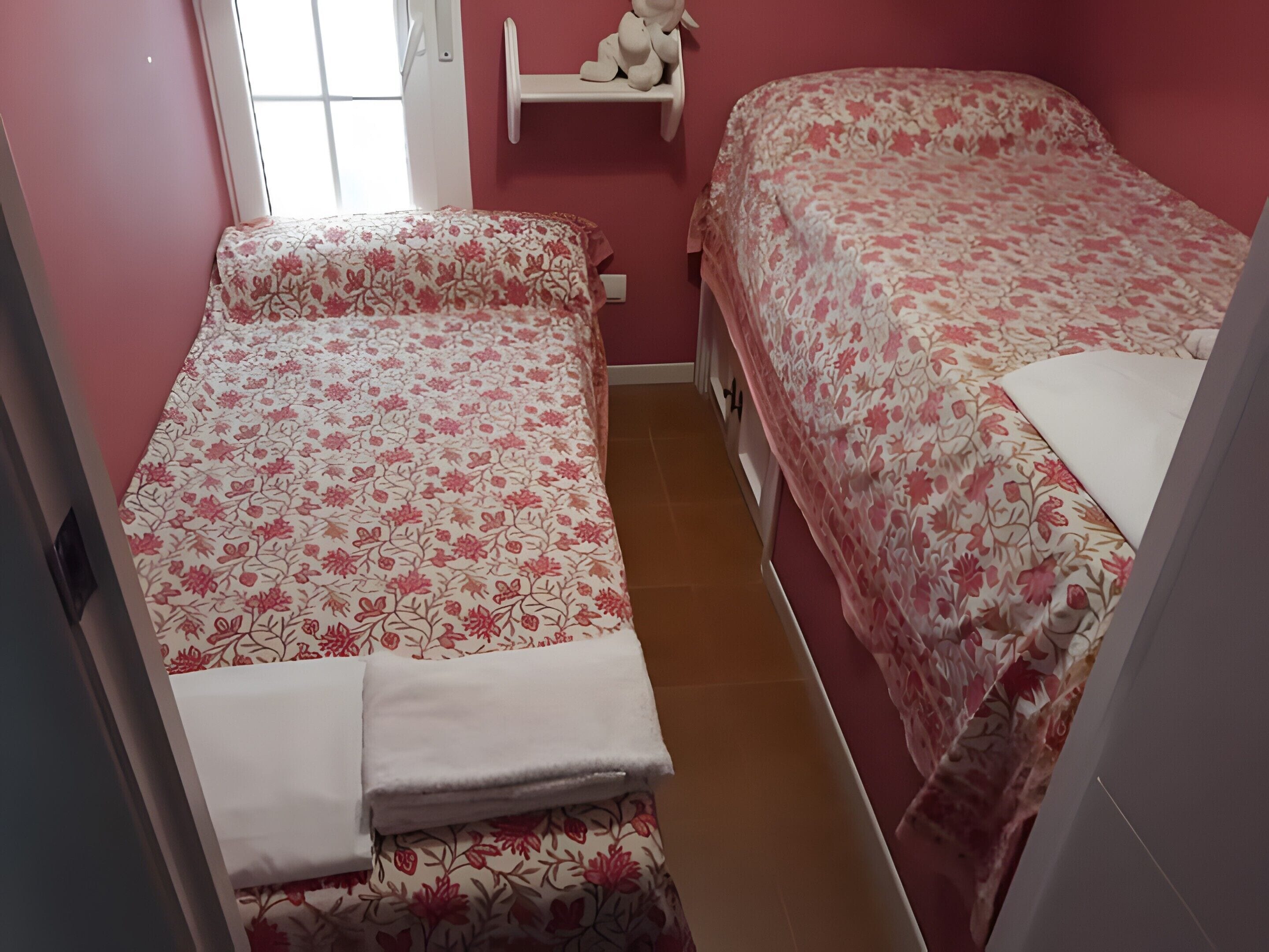 Un dormitorio con dos camas, una ventana y un estante con un oso de peluche.