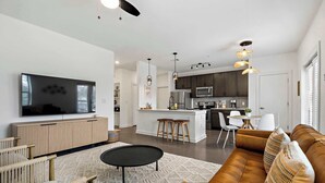 A modern living room with a sofa, coffee table, and TV. There is a kitchen in the background with a dining area. - South Lamar Condo / Sauna / Cold Plunge / Pickleball (Austin)