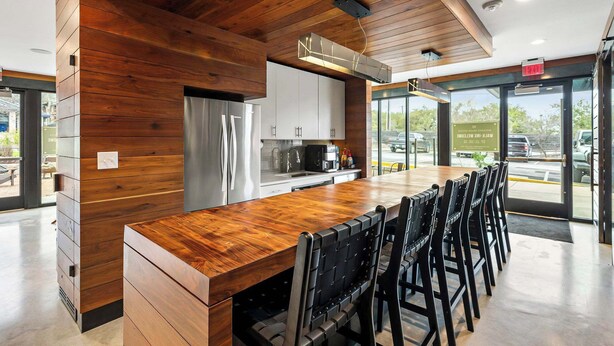 A modern kitchen with wooden paneling, stainless steel appliances, and a bar area with black chairs. - South Lamar Condo / Sauna / Cold Plunge / Pickleball (Austin)